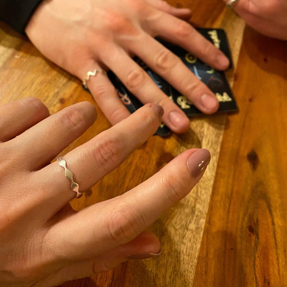 Zu sehen sind zwei Hände mit je einem Ring beim Kartenspielen. Der eine Ring im Vordergrund ist der Antiwave Small, der andere ist der Zickzack.