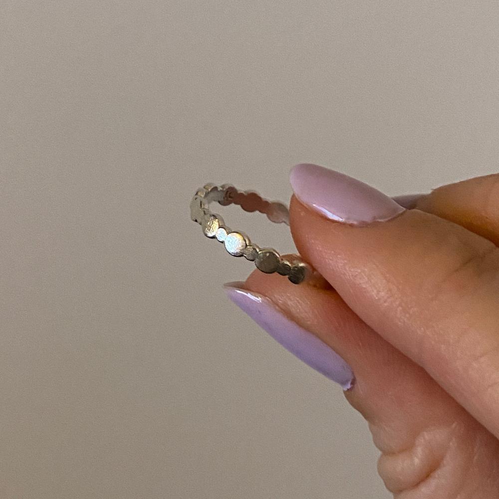 Zu sehen ist ein Silberring bestehend aus wechselnd großen und kleinen Perlen. Die Perlen sind flach und bilden das Band. Der Ring ist sehr minimalistisch.