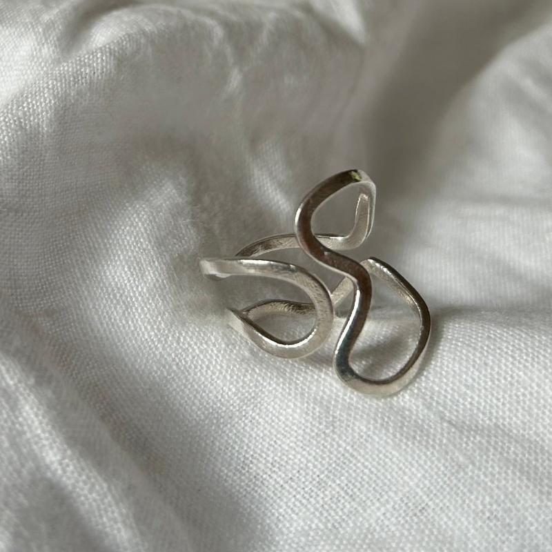 Der Ring auf dem Bild ist ein richtiger Eyecatcher. Er ist wie alle sehr minimalistisch gestaltet, jedoch bespielt er die gesamte Fläche zwischen Hand und Fingerknöchel. Er ist oben größenverstellbar. Eine Welle vorne greift in zwei Wellen von der anderen Seite.