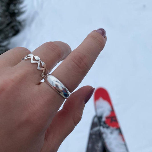 Zu sehen ist eine Hand mit Silberringen. Im Hintergrund sind Ski zu sehen. Die Ringe an der Hand sind der Loop No.2, der Zickzack und der Antiwave Small.