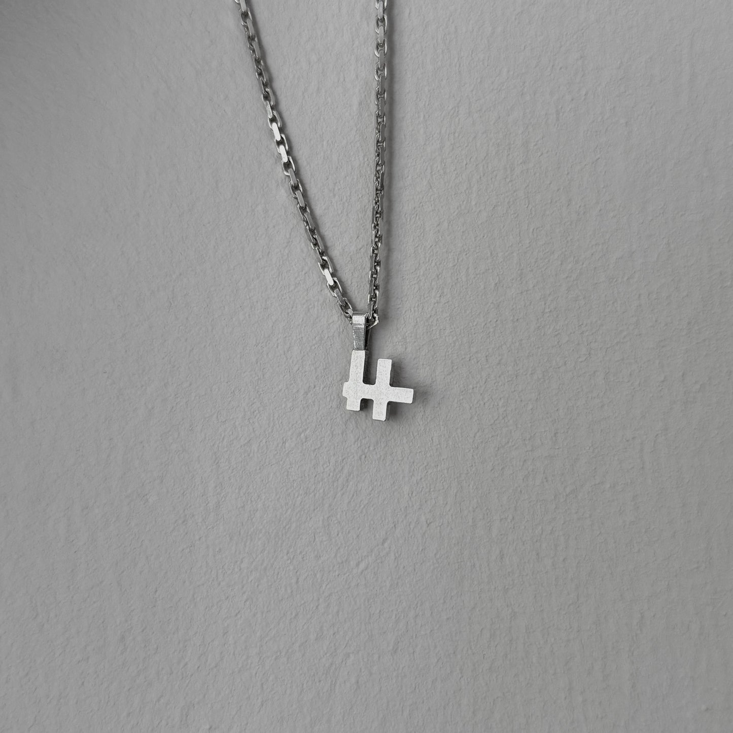Foto des Logo-Kettenanhängers an einer Kette vor einer grauen Wand.