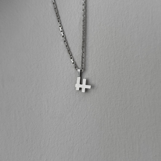 Foto des Logo-Kettenanhängers an einer Kette vor einer grauen Wand.