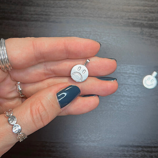 Auf dem Bild sieht man zwei Kettenanhänger. Einen mit einem glücklichen, den anderen mit einem traurigen Smiley. Es handelt sich jedoch um einen Kettenanhänger der von der einen Seite den happy und von der anderen Seite den sad Smiley hat. 925er Sterling Silber.