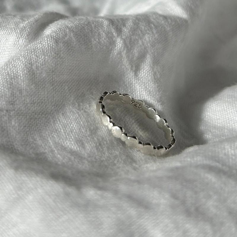 Zu sehen ist ein Silberring bestehend aus wechselnd großen und kleinen Perlen. Die Perlen sind flach und bilden das Band. Der Ring ist sehr minimalistisch.