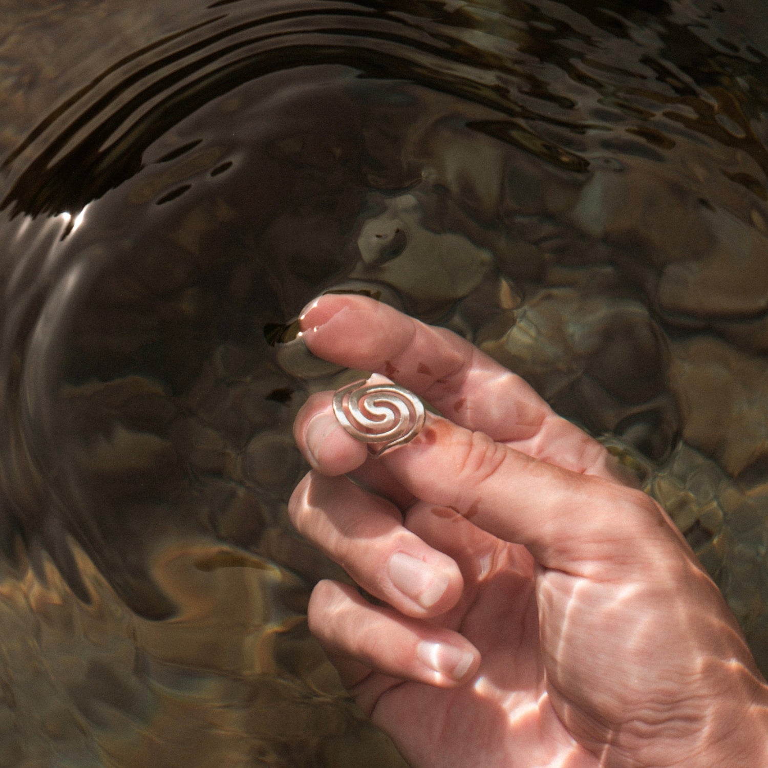 Zu sehen ist eine Hand unter Wasser. Sie hält den La Spezia Flow zwischen den Fingern. Der Zeigefinger löst leichte Wellen aus.