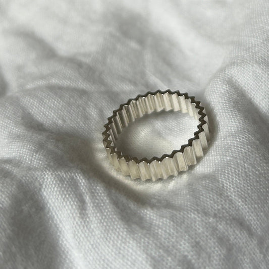 Ein Foto vom Tastsinntraining-Ring "TIA 03.1 Inside&Out Small" auf einem weißen, Leinenuntergrund. Der Ring hat eine zackige Form von außen und innen.