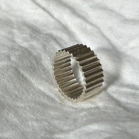 Ein Foto vom Tastsinntraining-Ring "TIA 03 Inside&Out Big" auf einem weißen, Leinenuntergrund. Der Ring hat eine zackige Form von außen und innen.