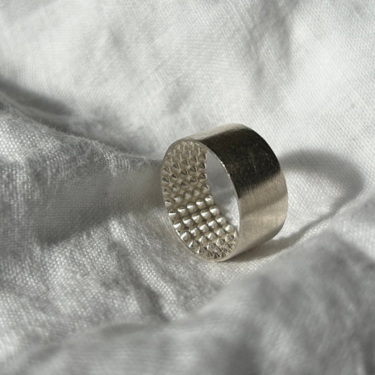 Ein Foto vom Tastsinntraining-Ring "TIA 01 Spikes" auf einem weißen, Leinenuntergrund. Der Ring hat einen glatten Look von außen und kleine Igelstachel (Wie bei einem Igelball) innen.