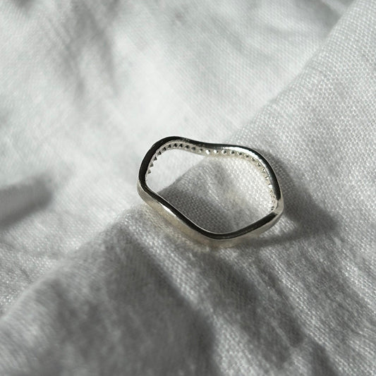 Ein Foto vom Tastsinntraining-Ring "TIA 05 Chiavari" auf einem weißen, Leinenuntergrund. Der Ring hat einen glatten, schlichten Look von außen (eine dünne Wellenform) und kleine Igelstachel (Wie bei einem Igelball) innen.